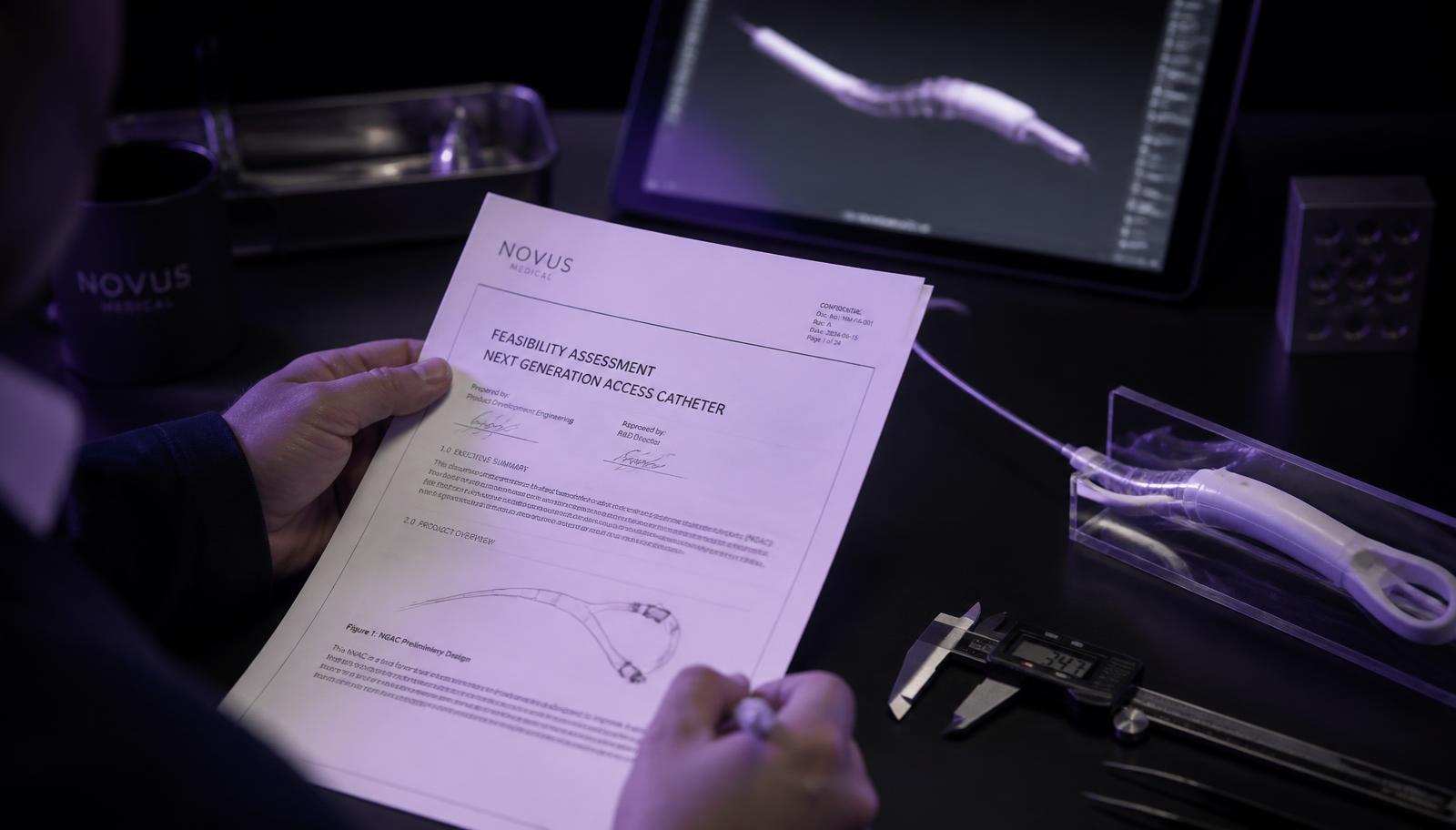 Engineer reviewing a medical device feasibility assessment document beside a prototype catheter